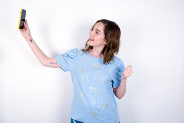 Portrait of a young caucasian woman wearing blue T-shirt over white background taking a selfie to send it to friends and followers or post it on his social media.