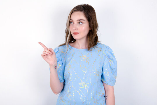 young caucasian woman wearing blue T-shirt over white background points at copy space and advertises something, advices best price.