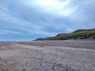 Dänischer Sandstrand bei bewölktem Himmer mit einigen grasbewachsenen Dünen