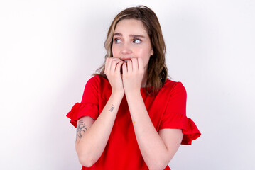 Terrified young caucasian woman wearing red T-shirt over white background looks empty space home alone moonless night