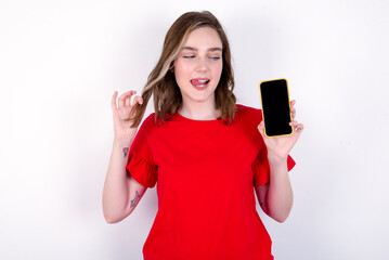 Fototapeta premium Photo of nice pretty young caucasian woman wearing red T-shirt over white background demonstrate phone screen hold hair tails