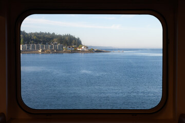 View through a rectangular ferry window of the Mukilteo shoreline and the blue water of Puget Sound