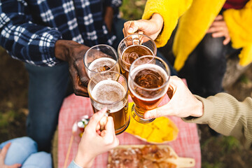 Closeup of multiethnic hands holding beer mugs and toasting together outdoors - Concept of multiracial young people gathering for happy hour drinking - main focus on the hand of the woman in yellow - obrazy, fototapety, plakaty