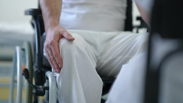 Unrecognizable worried man in wheelchair touching legs consulting doctor in hospital indoors. Anxious Caucasian male patient with paralysis hoping for brand new treatment in medical clinic