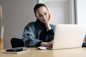Stylish young woman freelancer working online writes a message using a laptop, a workplace in the office