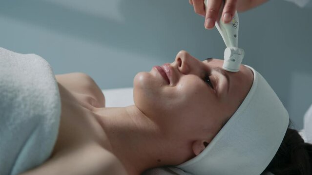 Attractive woman with prefect skin having facial procedures while lying at spa salon. Treatment of female face by special equipment. Ultrasound massage. Beautician using electrical impulses. Close-up