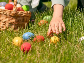 Fototapeta premium The child's hand reaches out to the Easter painted egg on the green grass. The Easter concept