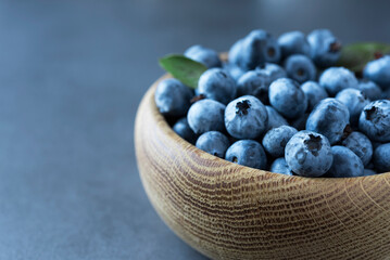 Ripe blueberry in the wooden bowl close up on the dark grey background. Copy space. Minimalism. Healthy nutrition