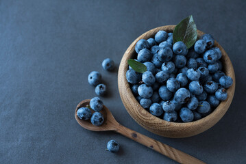 Wooden bowl and spoon with fresh bluberry on the dark grey background. Flat lay. Top view. Copy space. Minimalism. Healthy nutrition