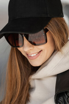 Fashion urban female portrait of beautiful trendy happy stylish woman hipster with smile with vintage sunglasses with black mock-up cap in beige hoodie walks in the city