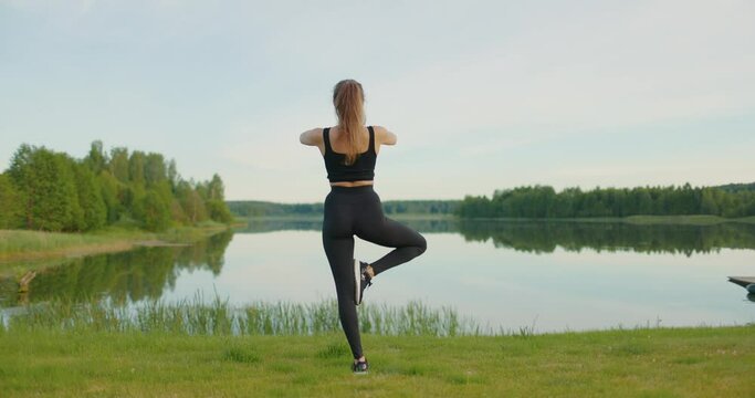 Young athletic woman practices yoga on lake shore. Slow motion
