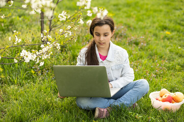 Little girl using laptop computer in a backyard. Child studying at home doing her homework or having online lesson. Homeschooling concept.