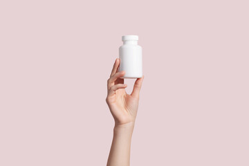 Young female hand holding blank white squeeze bottle plastic tube on pink background. Packaging for pill, capsule or supplement. Product branding mockup. - obrazy, fototapety, plakaty