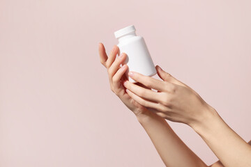 Young female hands holding blank white squeeze bottle plastic tube on pink background. Packaging...