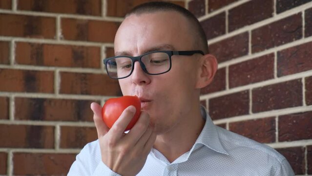 Young man eating fresh tomato, close-up