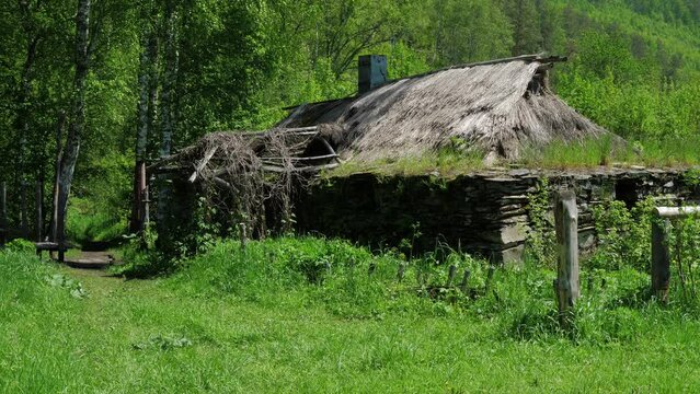 Fairy wooden house with chimney is in meadow next to trees. Abandoned old shack, hovel is in forest. Ancient dwelling of forester, hermit, dwarf, hobbit at wooded place. Sunny day