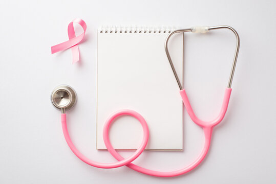 Breast cancer awareness concept. Top view photo of pink silk ribbon stethoscope and notepad on isolated white background with empty space
