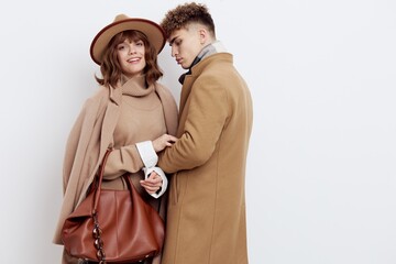 a happy couple in love is standing in beige stylish autumn coats on a white background and holding hands, a woman has a hat on her head and she is holding a bag in her hand
