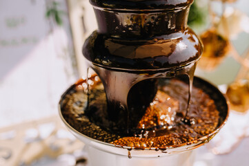 Hot brown milk melted chocolate is poured over the tiers of a fondue fountain close-up. Photo of food, dessert.