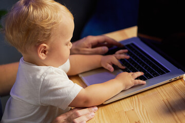 Young father working remotely on laptop with little baby son in his arms