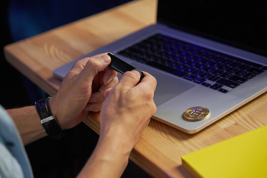A young male freelancer works remotely in a cafe on a laptop and holds a crypto wallet in his hands