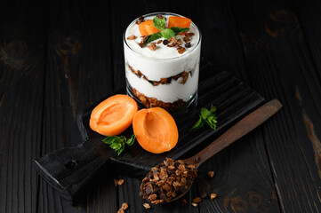 Homemade layered dessert with fresh apricot, cream cheese or yogurt, granola on rustic background.