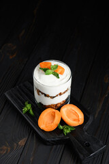 Homemade layered dessert with fresh apricot, cream cheese or yogurt, granola on rustic background.