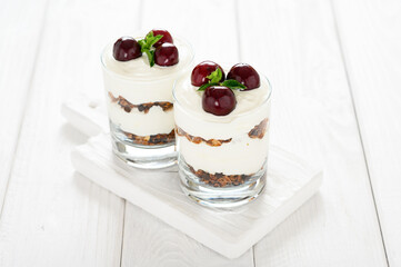Dessert with cheese, fresh cherries and granola in a glass on a white wooden background.