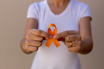 woman in white t-shirt holding orange ribbon. skin cancer prevention campaign