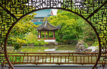 Looking through ginko wood latus design at a traditional chinese pagoda and a bridge with reflection pond in a chinese garden in  Chinatown in in downtown Vancouver, BC, British Columbia, Canada