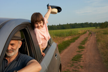 A fragment of a car on a field road with an adult man driving and a happy little girl in the back...