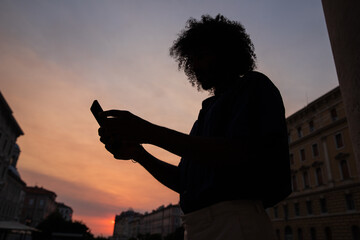 silhouette of a guy with afro using his smartphone during sunset in the city center.