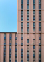 Obraz premium close up of a modern concrete highrise concrete building with geometrical repeating windows with angular details and corner showing blue sky
