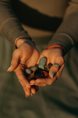 A close photo of a bunch of colorful stones in the hands of a woman for magical therapy. Session of a meditation healing in the park at sunset.