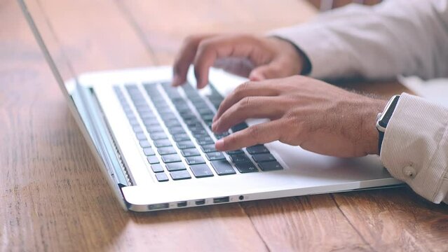 Man hands typing on keyboard of silver laptop performing work of office employee or secretary filling out online forms or writing business letter for partners and company staff . Close-up