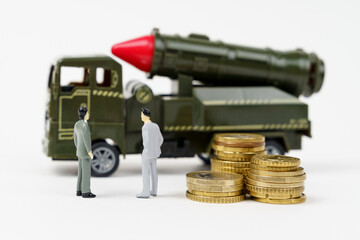 On a white surface are figurines of people, coins and a toy military vehicle.