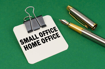 On a green surface, a pen and a sheet of paper with the inscription - Small Office Home Office