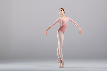 Beautiful ballerina on a white background. The ballerina is dressed in a light pink lace leotard,...