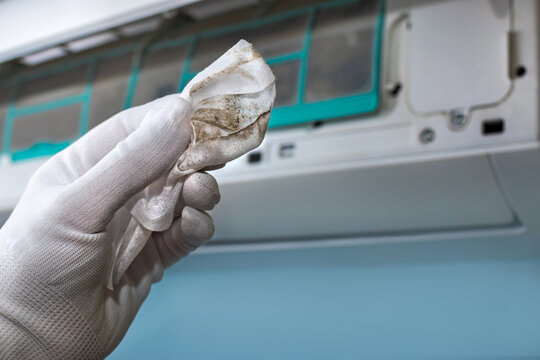 A man holds a dirty napkin in his hand against the background of an air conditioner. Split system maintenance