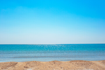Fototapeta na wymiar Blue sparkling sea with a strip of sandy shore and a clear blue sky on a sunny day