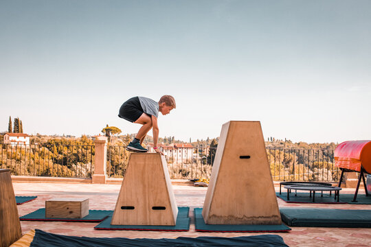 Parkour athletic challange. Young caucasian boy is jumping over trapezoidal blocks, fitness competition, outdoor sport summer camp