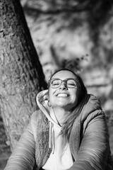 Chica europea con gafas y chaqueta en invierno con los ojos cerrados sonriendo hacia arriba con sol en la cara en un bosque