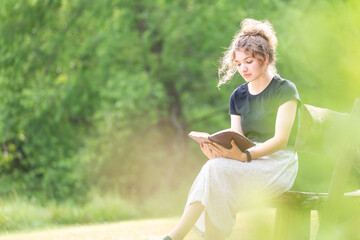 Young woman reading Bible on bench - Powered by Adobe