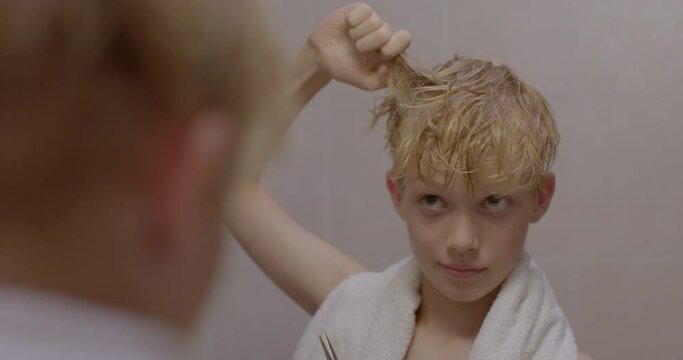 Boy cuts hair on his own while looking in bathroom mirror. Teenager in search of his style. Boys begin puberty sometime between the ages of 9 and 14.