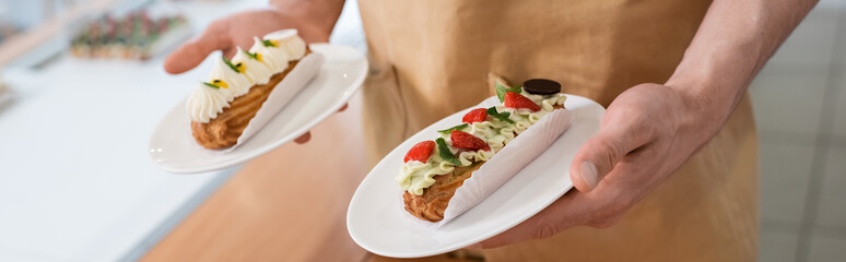 Cropped view of seller holding eclairs in confectionery, banner.