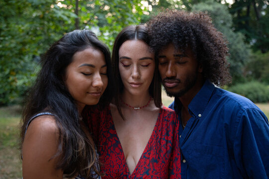 Three young people of different ethnicities pose with closed eyes, diversity and peace concept.
