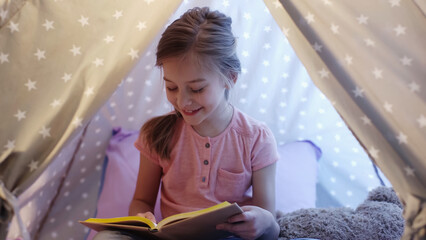 Happy preteen kid reading book in wigwam at home. © LIGHTFIELD STUDIOS