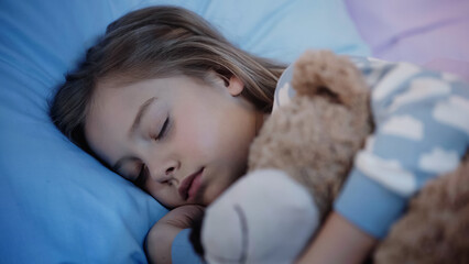 Preteen child hugging blurred teddy bear while sleeping on bed.