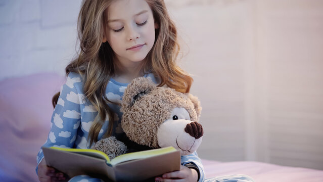 Preteen kid holding soft toy while reading book in bedroom.