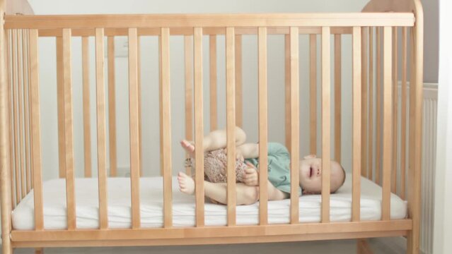 crying baby boy child kid lying in brown crib cot rolling, crawling, trying to sleep. caucasian toddler doesn't want or falling asleep, alone in cradle. childhood, parenthood, lonely getting to sleep 
